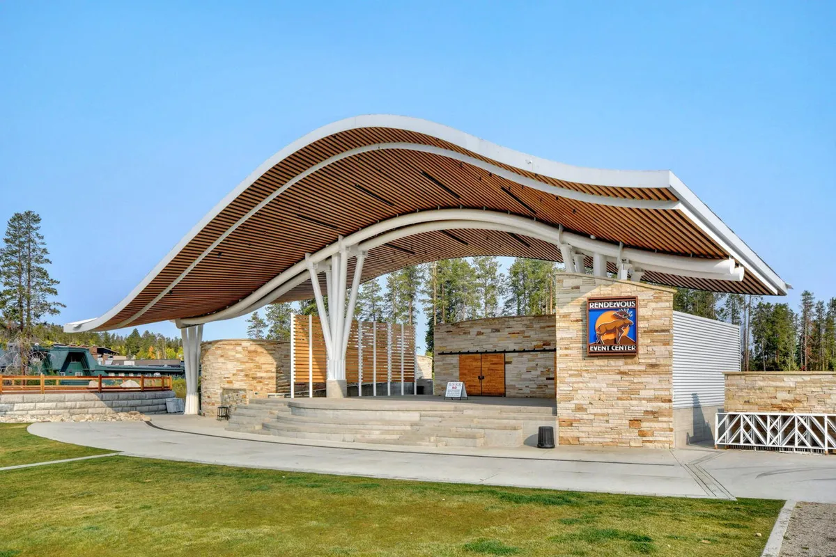 This exterior photograph captures the distinctive curved roof structure and stone walls of an outdoor event venue in Winter Park. The open space is set up for community gatherings, with event signage visible, and the area is bathed in warm, welcoming light—suggesting a festive atmosphere perfect for concerts or seasonal festivals.