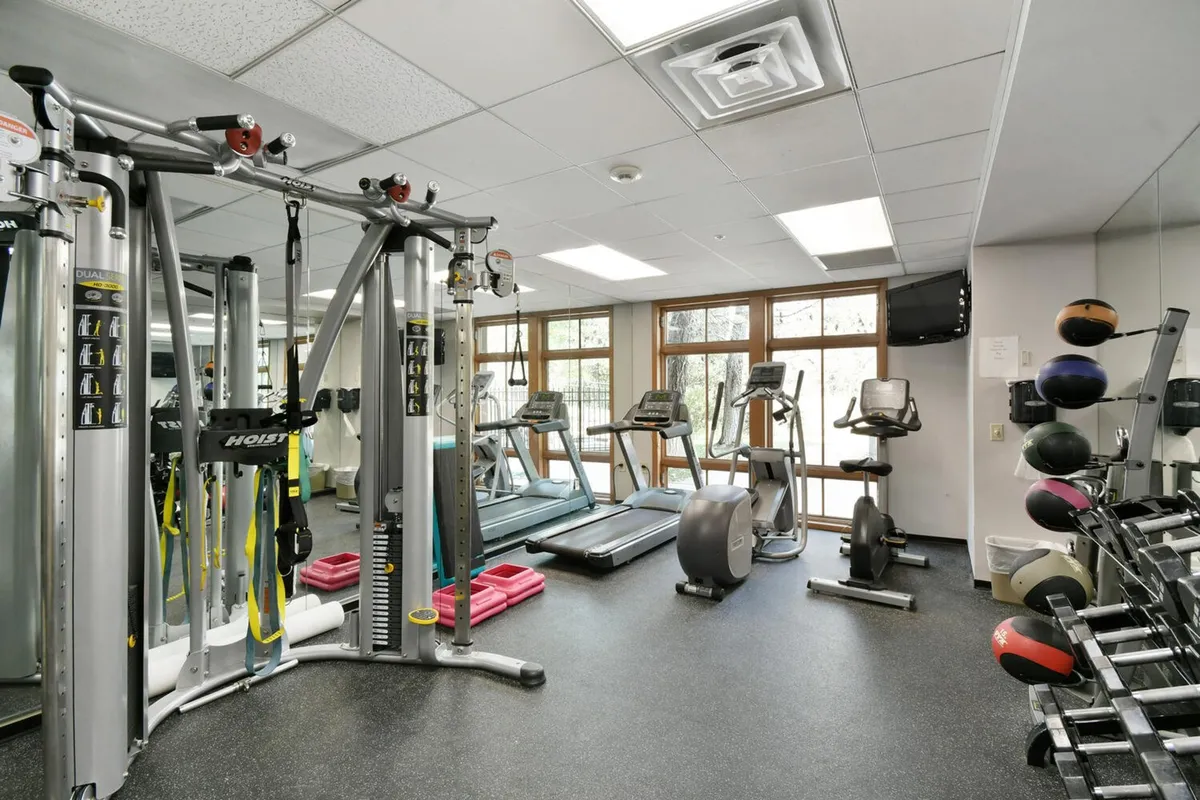 A well-equipped gym with a range of exercise machines, large windows letting in natural light, and a weights rack. The energetic mood encourages health and wellness, with views to the outdoors enhancing the modern fitness experience.