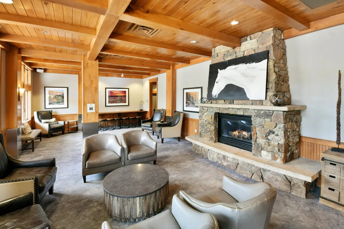 A cozy lodge interior featuring a welcoming fireplace surrounded by comfortable seating, warm wooden beams, and tasteful artwork. The inviting ambiance suggests a perfect place for guests to relax, socialize, or enjoy a quiet moment after a day of adventure.
