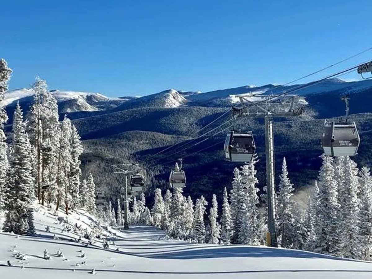 This exterior image features a ski lift ascending over snow-covered mountains, surrounded by pine trees. The scene captures the heart of the Winter Park Resort's ski-in/ski-out experience, with the gondola in action and pristine powder awaiting. The overall mood is adventurous and serene, conveying the thrill of immediate slope access and the stunning alpine environment.