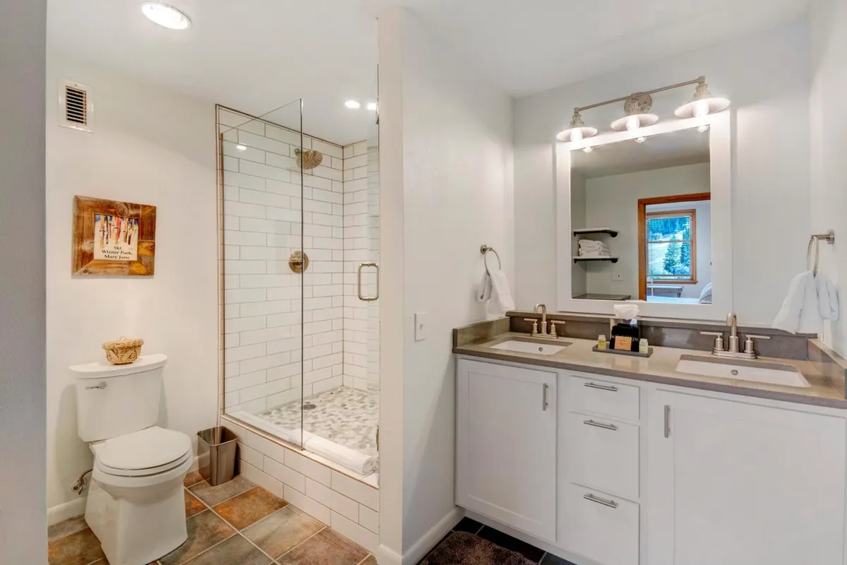 A modern bathroom with a glass shower enclosure, double vanity, and framed artwork creates a spa-like, serene retreat. The fixtures are sleek, and the space is inviting for relaxing routines after a day of adventure.