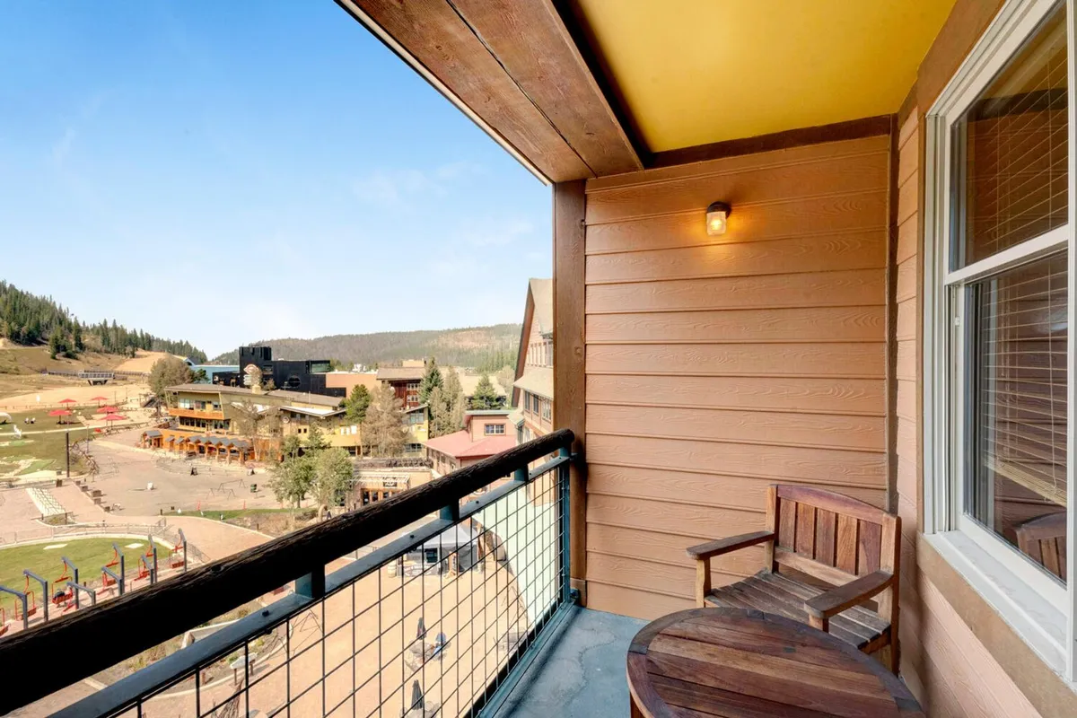 A peaceful outdoor scene from a covered balcony or deck, with a wooden chair facing the mountains and the outdoor area. The balcony provides the perfect spot for morning coffee, après-ski relaxation, or storytelling sessions with a panoramic view.